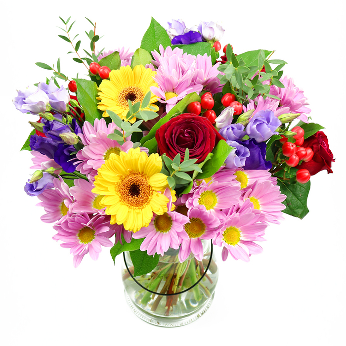 A vibrant, garden-style bouquet rises from a simple clear glass vase, set against a bright white background that lets every colour sing. At the centre, deep crimson red roses draw you in, their velvety petals curled in generous layers that suggest romance and warmth. Just off centre, golden yellow gerbera daisies radiate carefree energy, their neatly arranged petals circling those distinctive brown-orange centres that resemble tiny sunbursts. Spilling outward from these focal blooms is an abundant ring of pink and lavender daisies or chrysanthemums, their many slender petals and little yellow eyes forming a soft, cushion-like halo of pastel colour. Winding between the daisies, graceful lisianthus in shades of violet and pale lilac add depth and cool contrast, their elegant, bell-shaped flowers and slender buds giving the bouquet a gentle, flowing rhythm. Dotted among the petals, plump red hypericum berries offer flashes of glossy colour and a pleasing, rounded texture that feels almost jewel-like. The whole arrangement is enfolded in layers of mixed greenery: broader, darker leaves provide structure, while lighter, more delicate sprigs bring a sense of natural lift, much like the fresh foliage you might notice strolling through Slade Gardens on a bright morning. The clear vase allows the neatly cut stems and clean water to be clearly seen, reflecting the attentive craftsmanship of local Stockwell florists. Balanced between exuberant and elegant, this bouquet suits everything from heartfelt thank-yous and congratulations to a comforting surprise delivery for a friend along Clapham Road or near the Stockwell Underground, filling their space with colour and quiet joy.